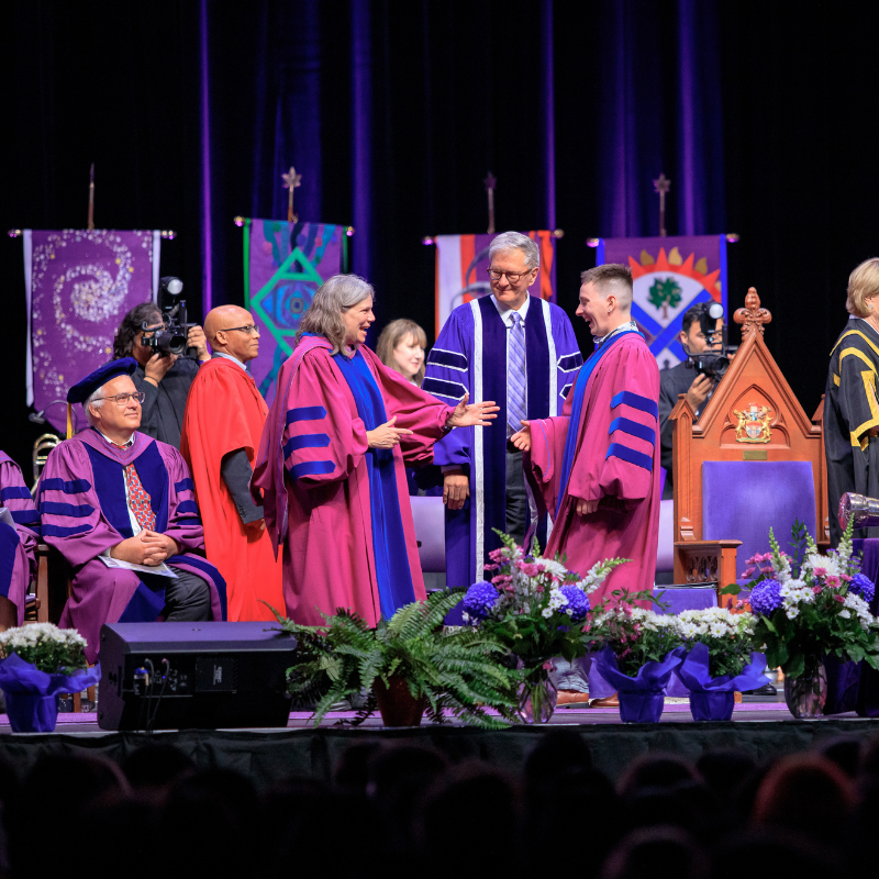 Staff sitting on the stage at convocation smiling and applauding
