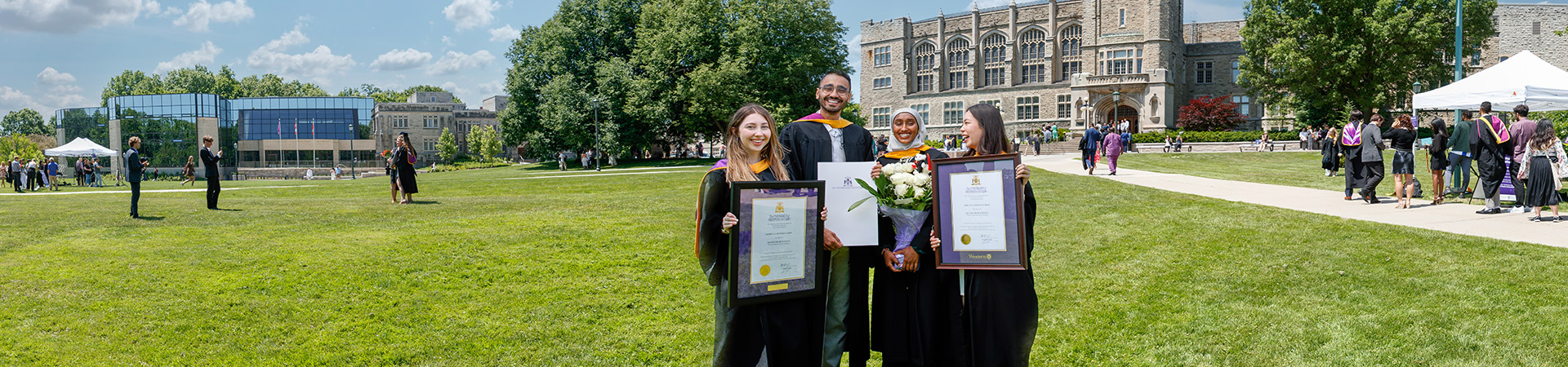 Four graduates with their diplomas on UC Hill