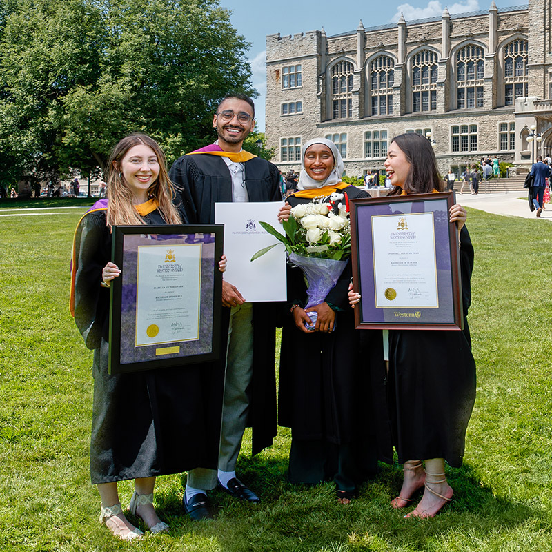 Four graduates with their diplomas on UC Hill
