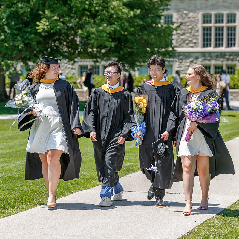 Four students walking in their robes down UC hill