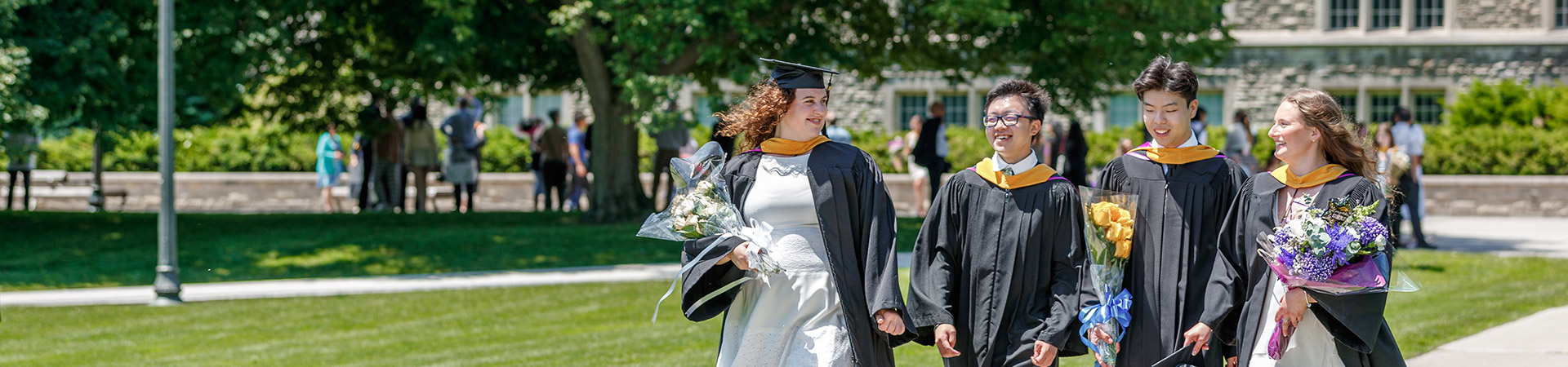 Four students walking in their robes down UC hill