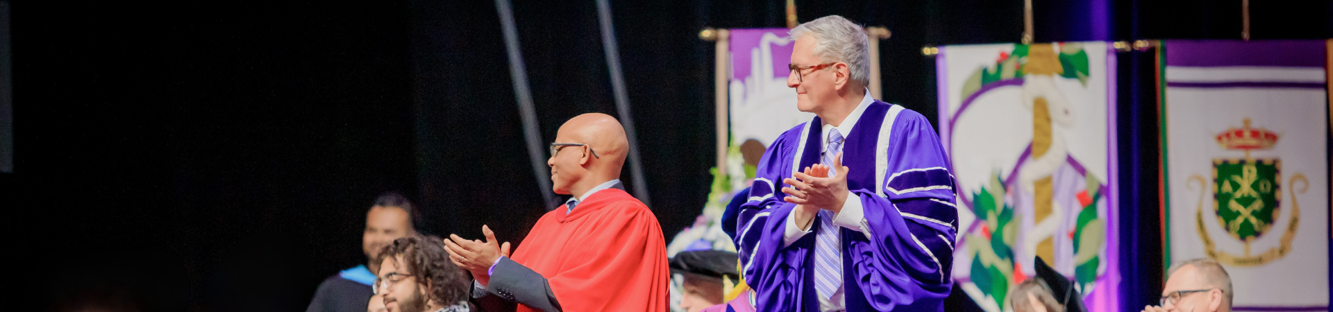 Two people standing on the Convocation stage appluading