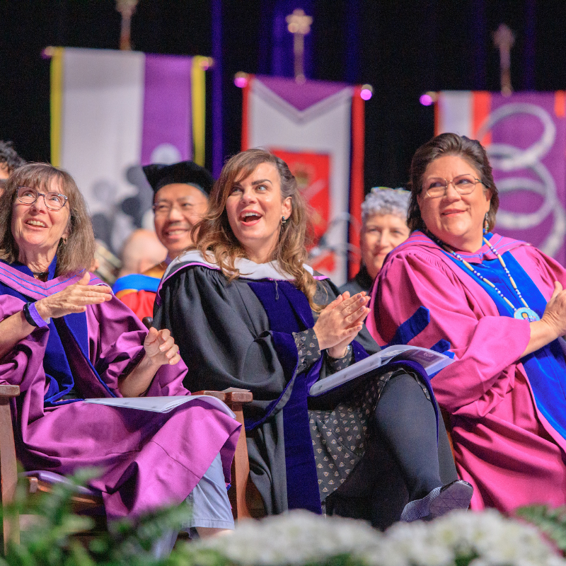 Staff sitting on the stage at convocation smiling and appluading