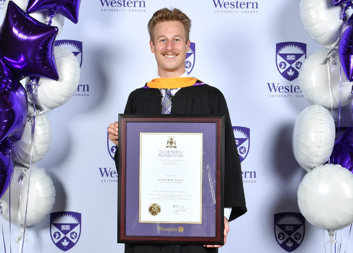 A graduate posing against a western backdrop with their dergee