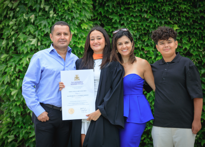 A graduate posing in front of a leafy background with their family