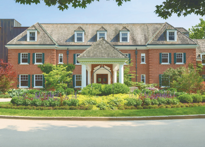 The front of the Spencer Hotel, a historic red brick building with bright gardens and trees in front of the enterance