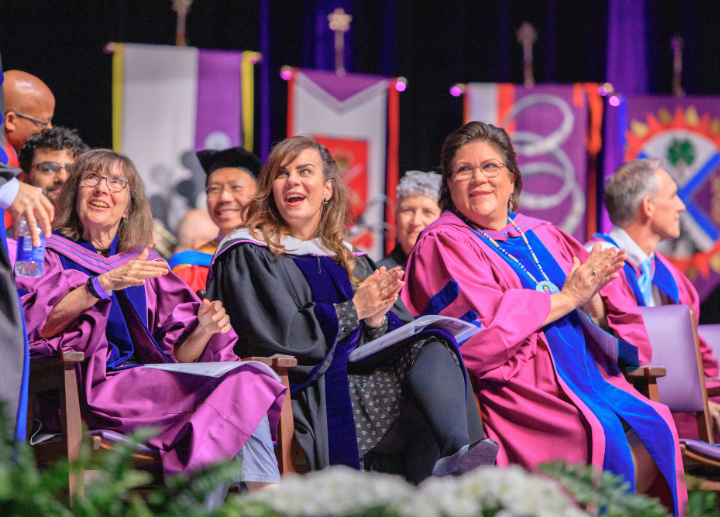 Staff on stage at convocation clapping for graduates as they cross the stage