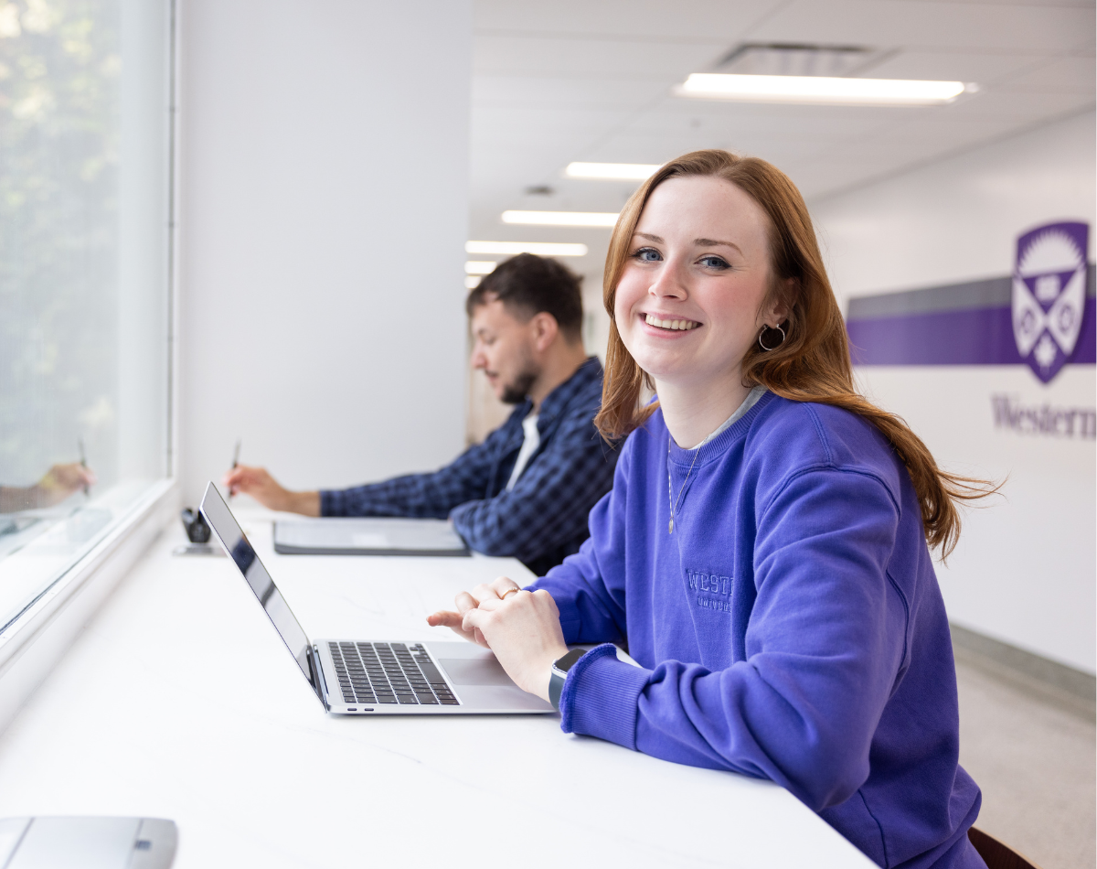 A female student sitting in a bright study space looking at a laptop